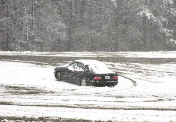 A black Mercedes sedan drifts in the snow.