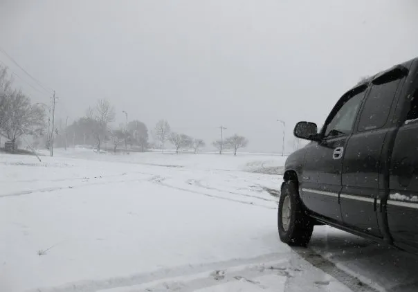 A black truck in the foreground. A snowy hill in the distance.