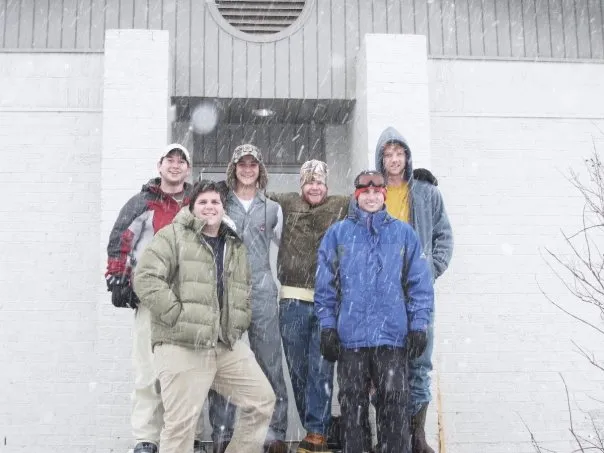 Friends pose in front of the fraternity house while it is snowing.