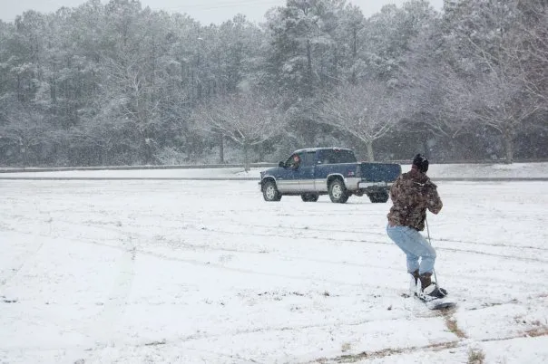 Someone gets pulled on a snowboard behind a blue truck.