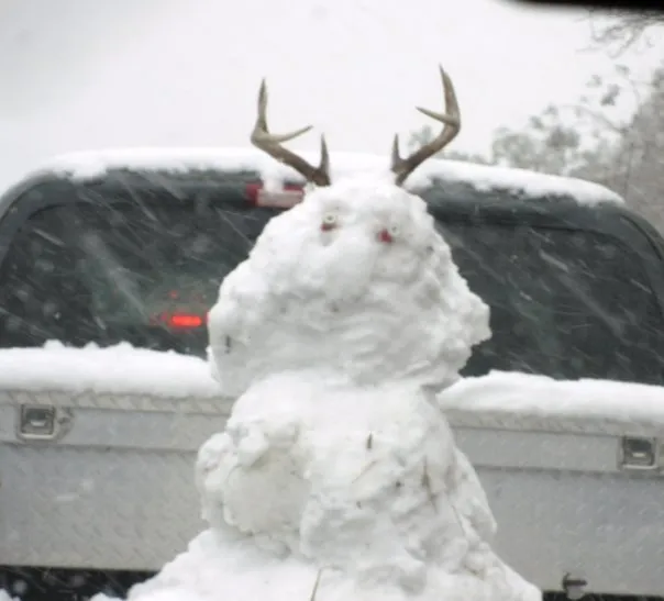 A snowman with antlers in the back of a pickup truck.