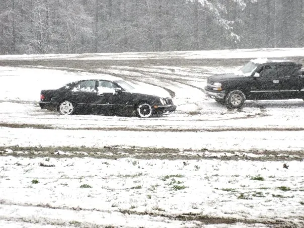 A black mercedes and black pickup truck drift in the snow.