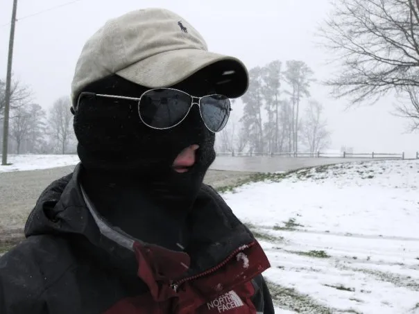 Andres with a ski mask, sunglasses and a hat out in the cold.