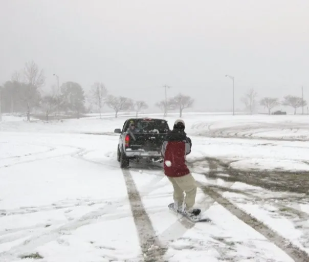 A truck pulling someone on a snowboard in the snow.