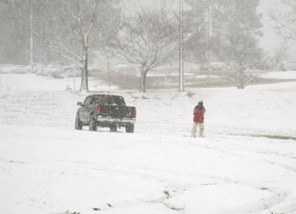 A black truck pulls someone behind it with a snowboard attached.