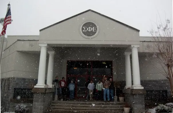 Front of the fraternity house with brothers posing while it is snowing.