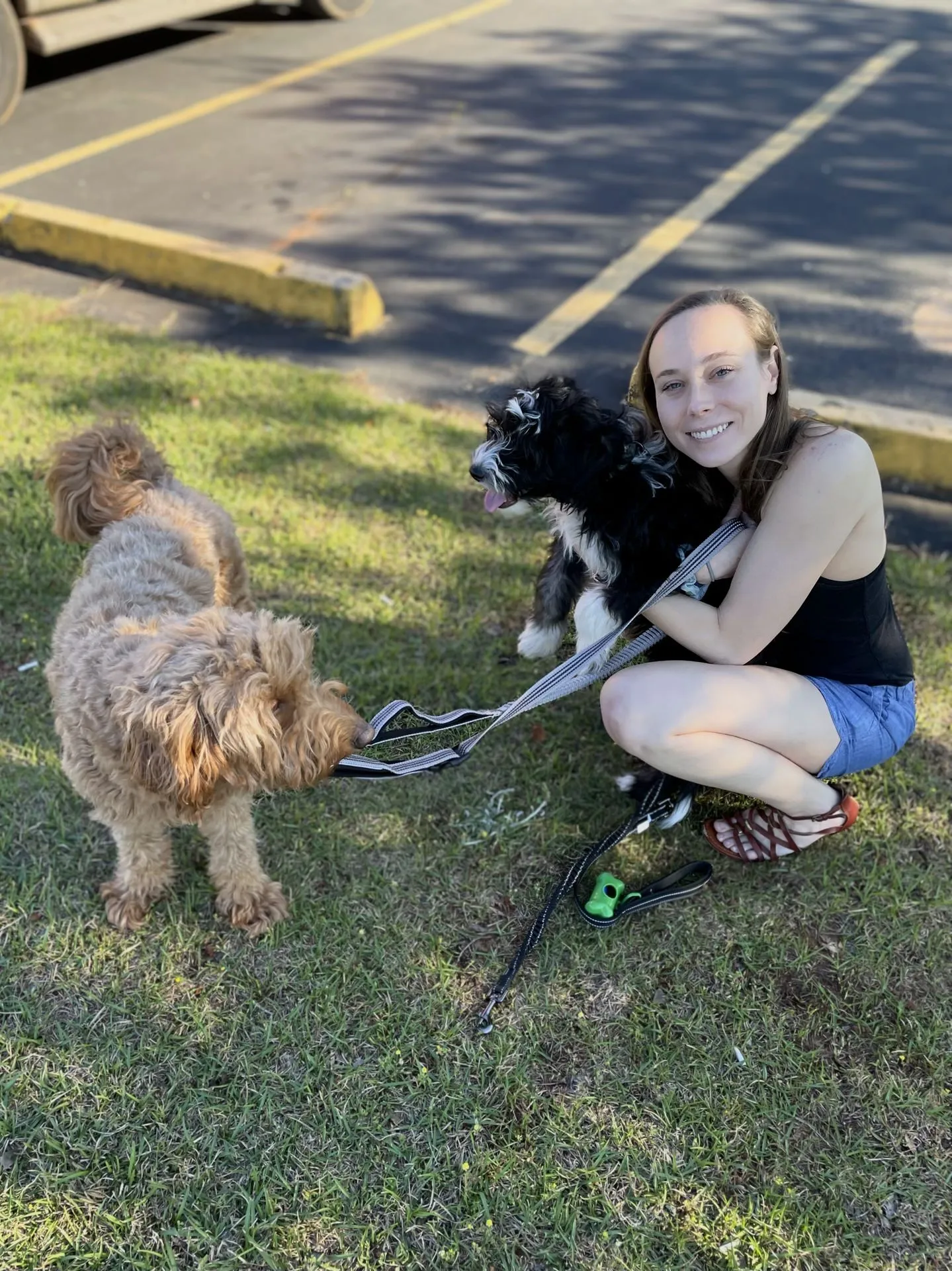 Holly crouches in a black top, holding Otto, a sheepadoodle puppy tightly. Otto has his tongue out. Remi looks at both of them skeptically.