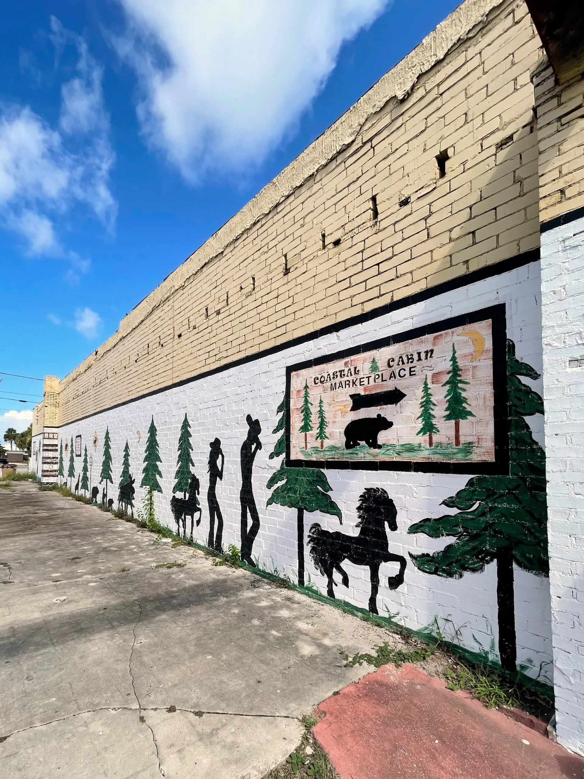 A mural of trees and horses on and old brick wall in downtown.