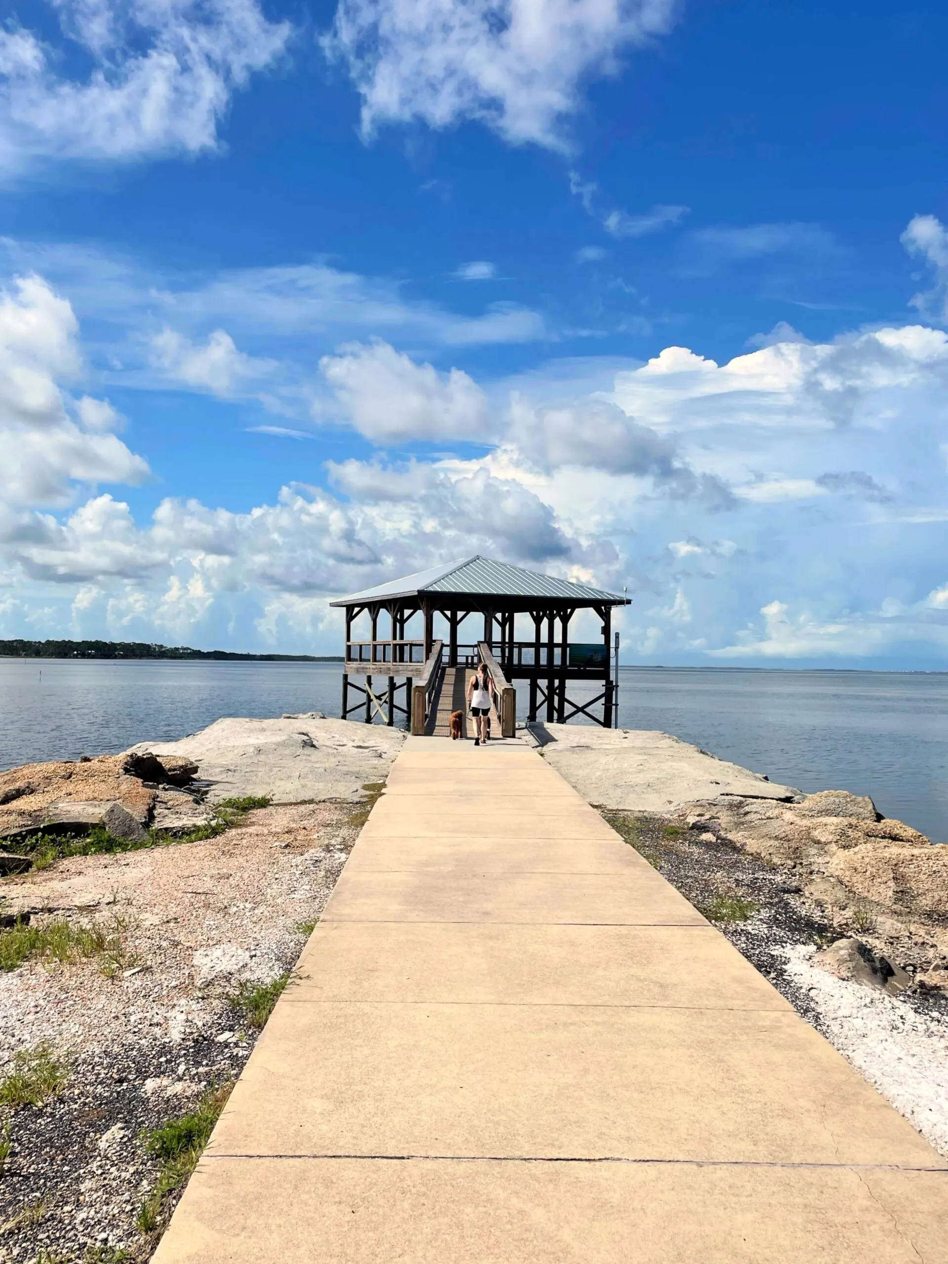 A large gazebo over the water. Holly and the dogs are centered walking on a path towards it.