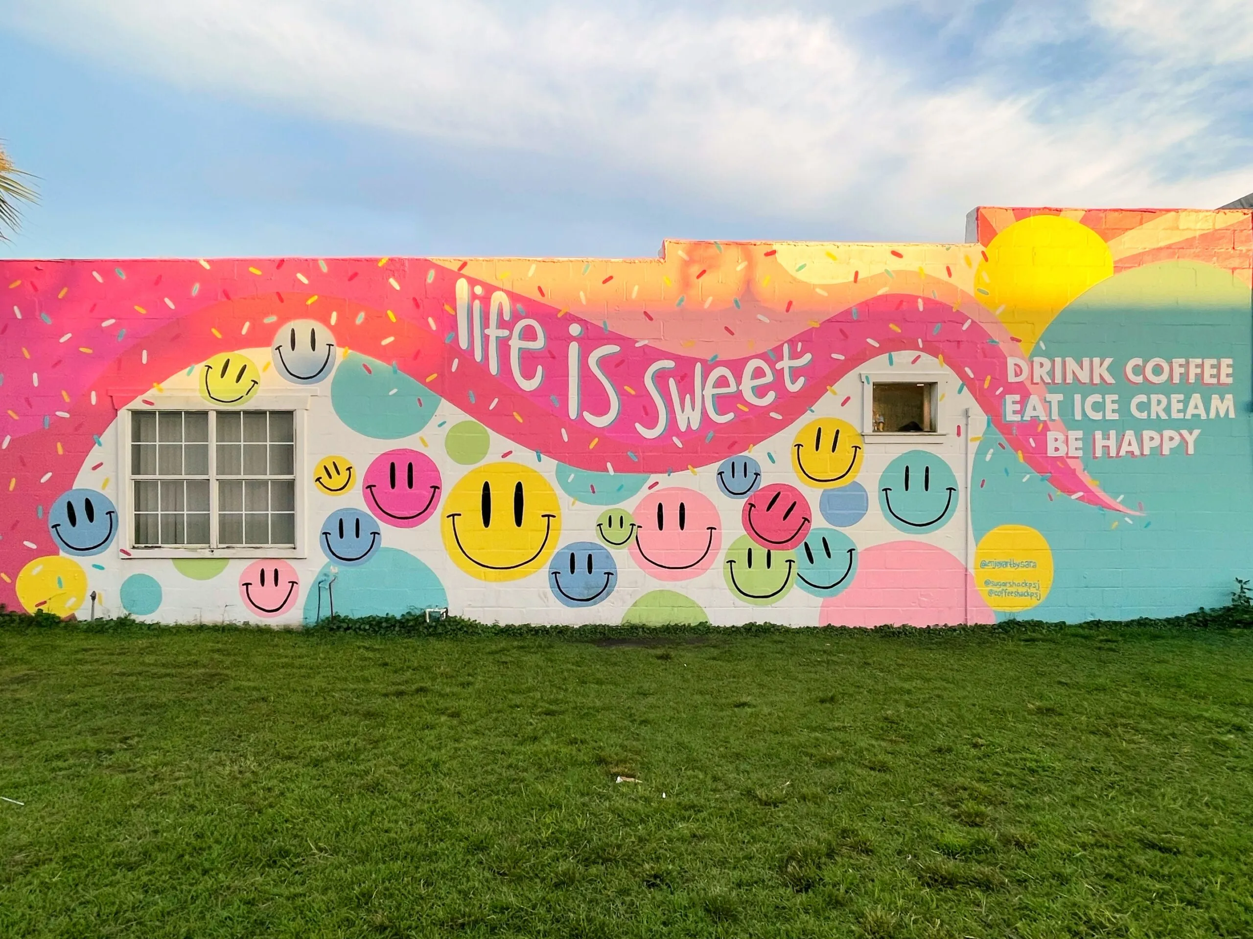 A colorful pink building decorated with smily faces and sprinkles. One side says "Life is sweet." The other says "Drink coffee. Eat Ice Cream. Be happy."